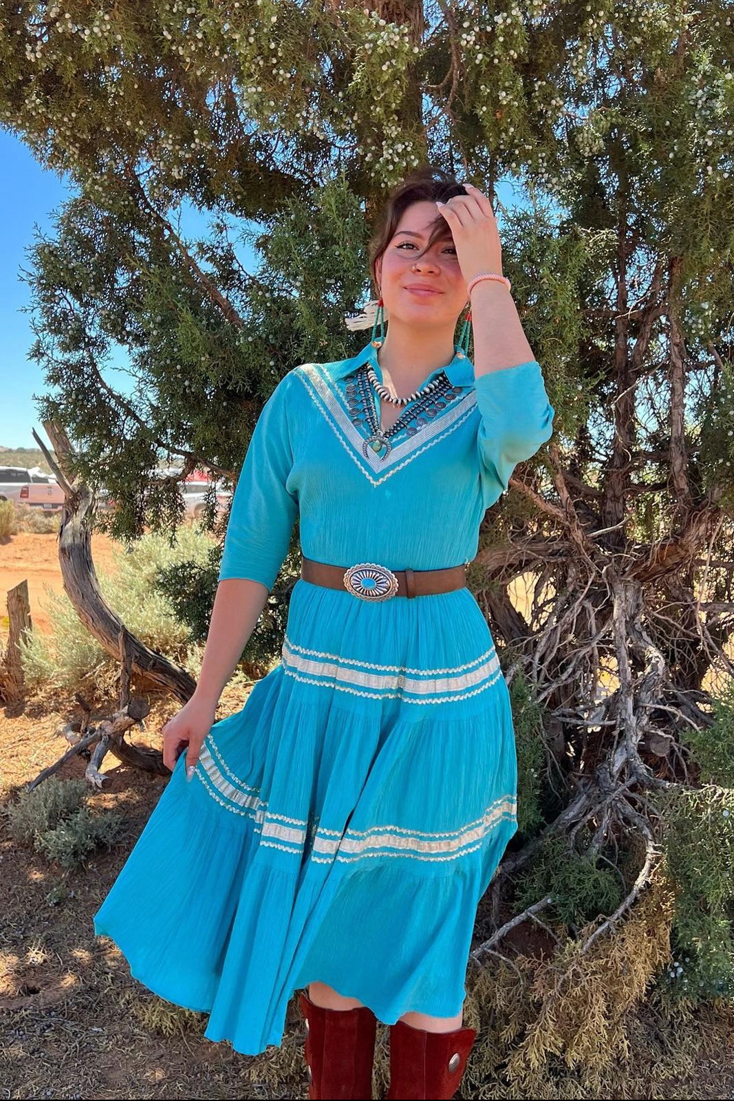 Hueston stands in against a juniper tree in the desert wearing a turquoise dress
