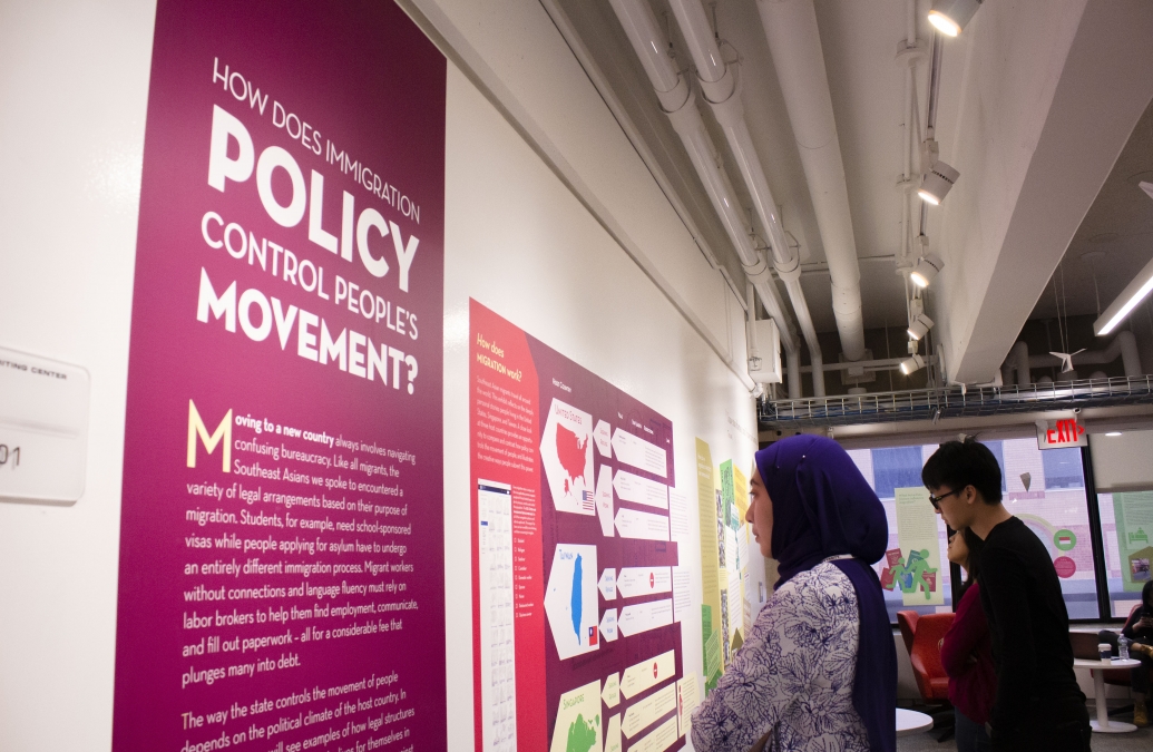 Two YSEALI fellows studies a wall display in an exhibition that reads "How does immigration policy control people's movement?"