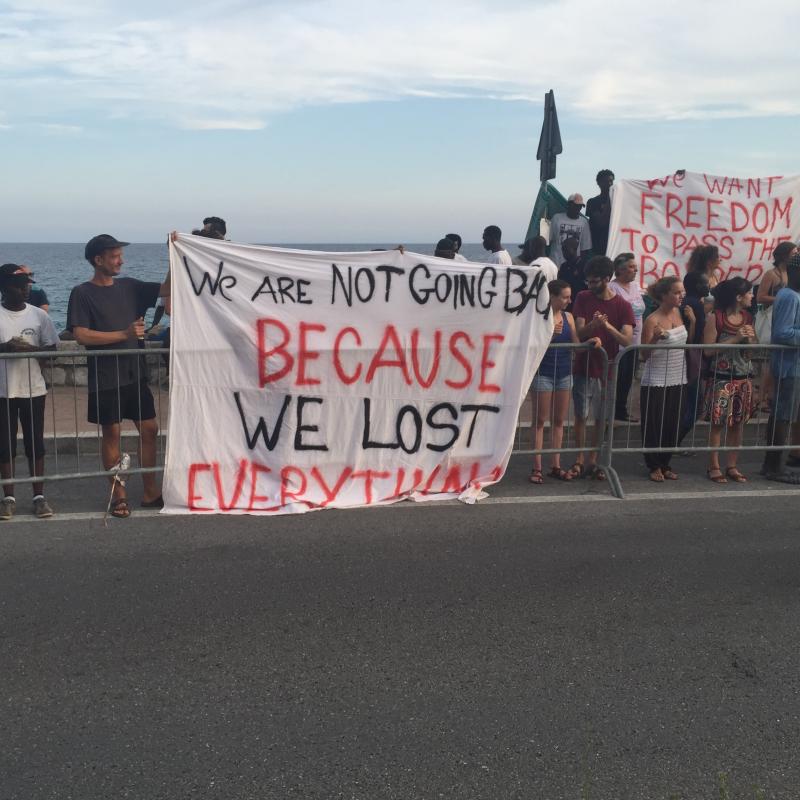 Refugees protest with banner that say "We are not going back because we lost everything."