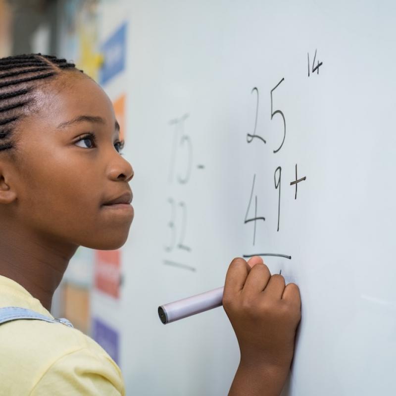 African American female student solving equation on white board in classroom