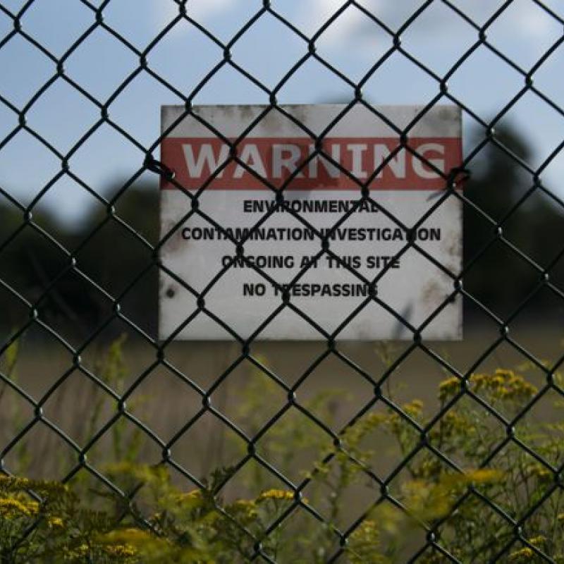 photo of fence with warning sign about environmental hazards