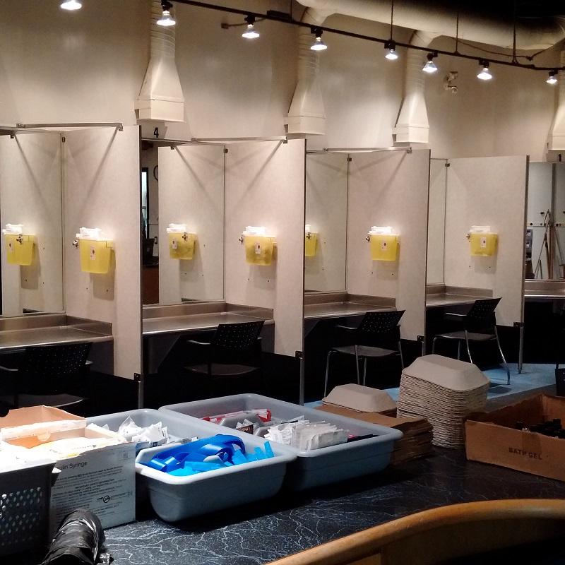 Photo of a supervised injection site showing several booths with behind a table of narcotic consumption supplies