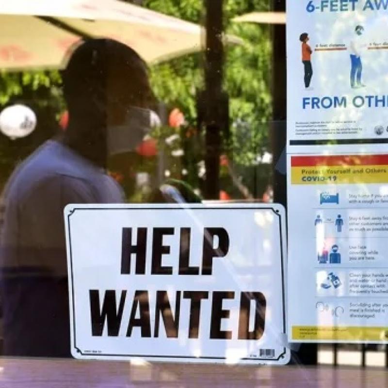 man wearing medical mask waiting behind a "Help Wanted" sign