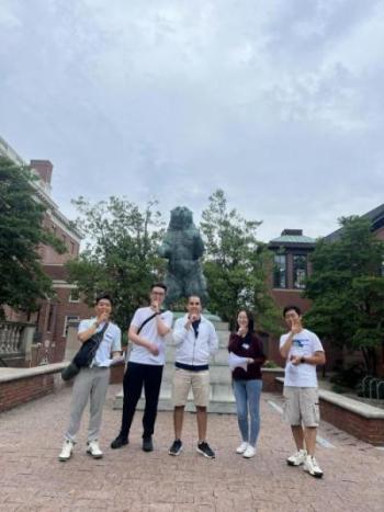 Five students in front of a bear statue holding one finger to their lips in a "shhh" gesture