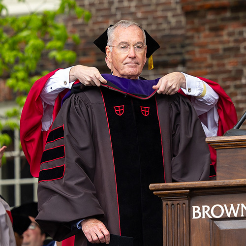 a person in graduation regalia on a stage being hooded