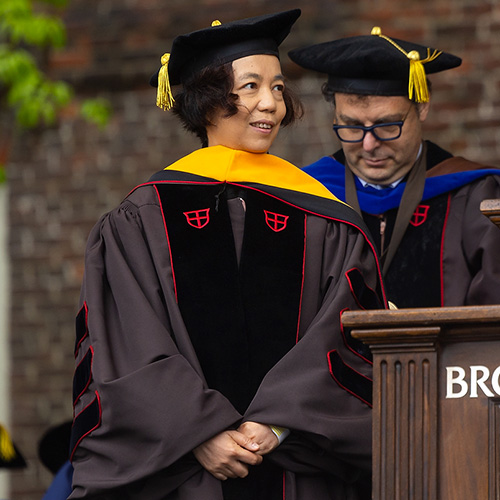 a person in graduation regalia on a stage being hooded