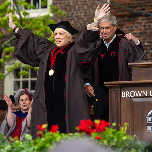 people in graduation regalia on a stage being hooded