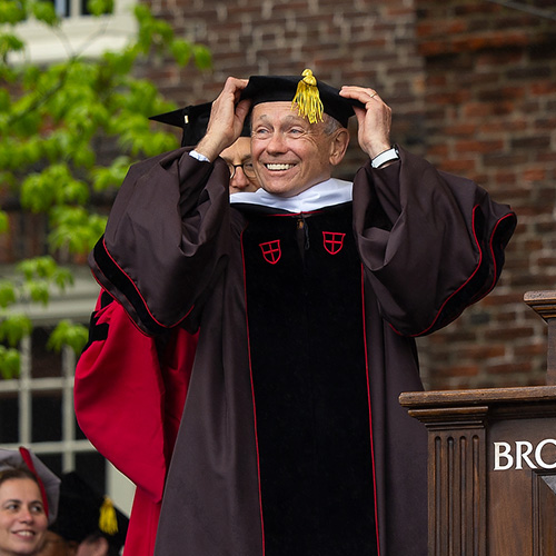 a person in graduation regalia on a stage being hooded