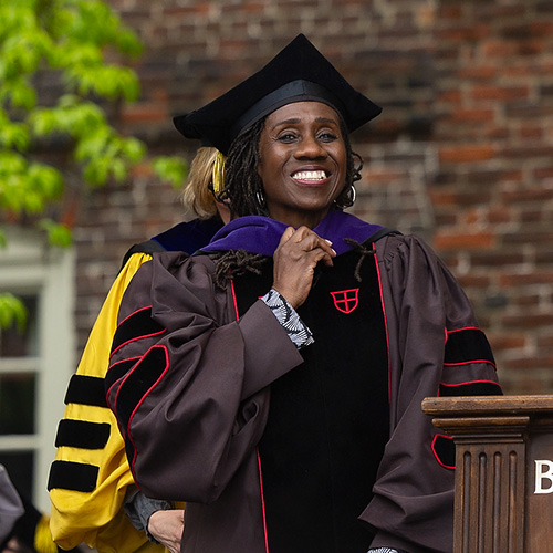 a person in graduation regalia on a stage being hooded