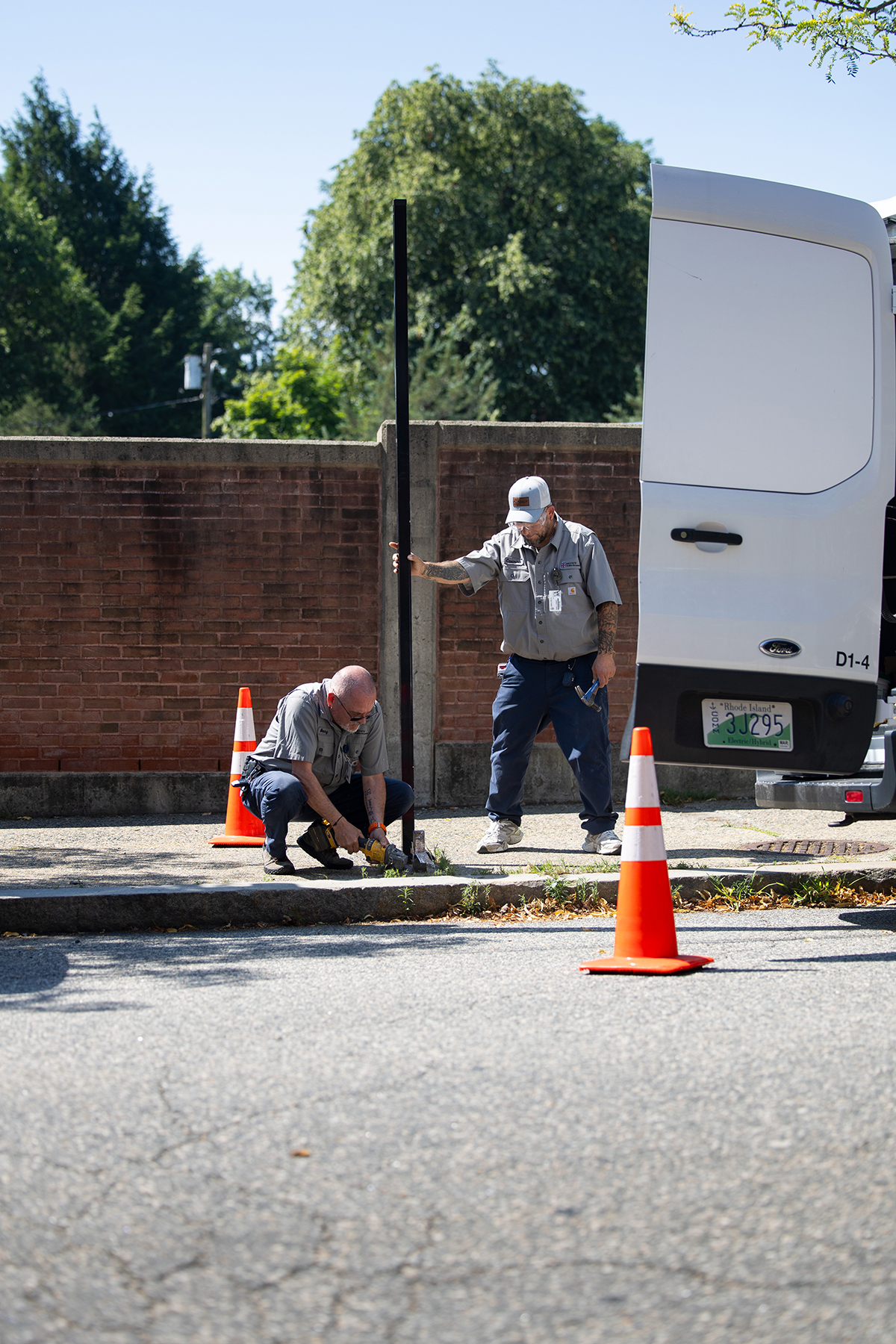 Two Brown facilities workers stand together to erect a new sign on a sidewalk on campus.