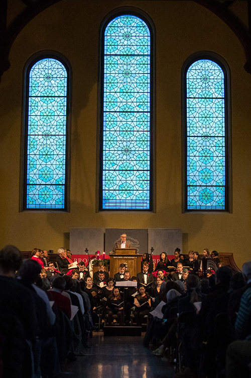 Large blue stained glass windows overlooking Richard Locke standing at podium