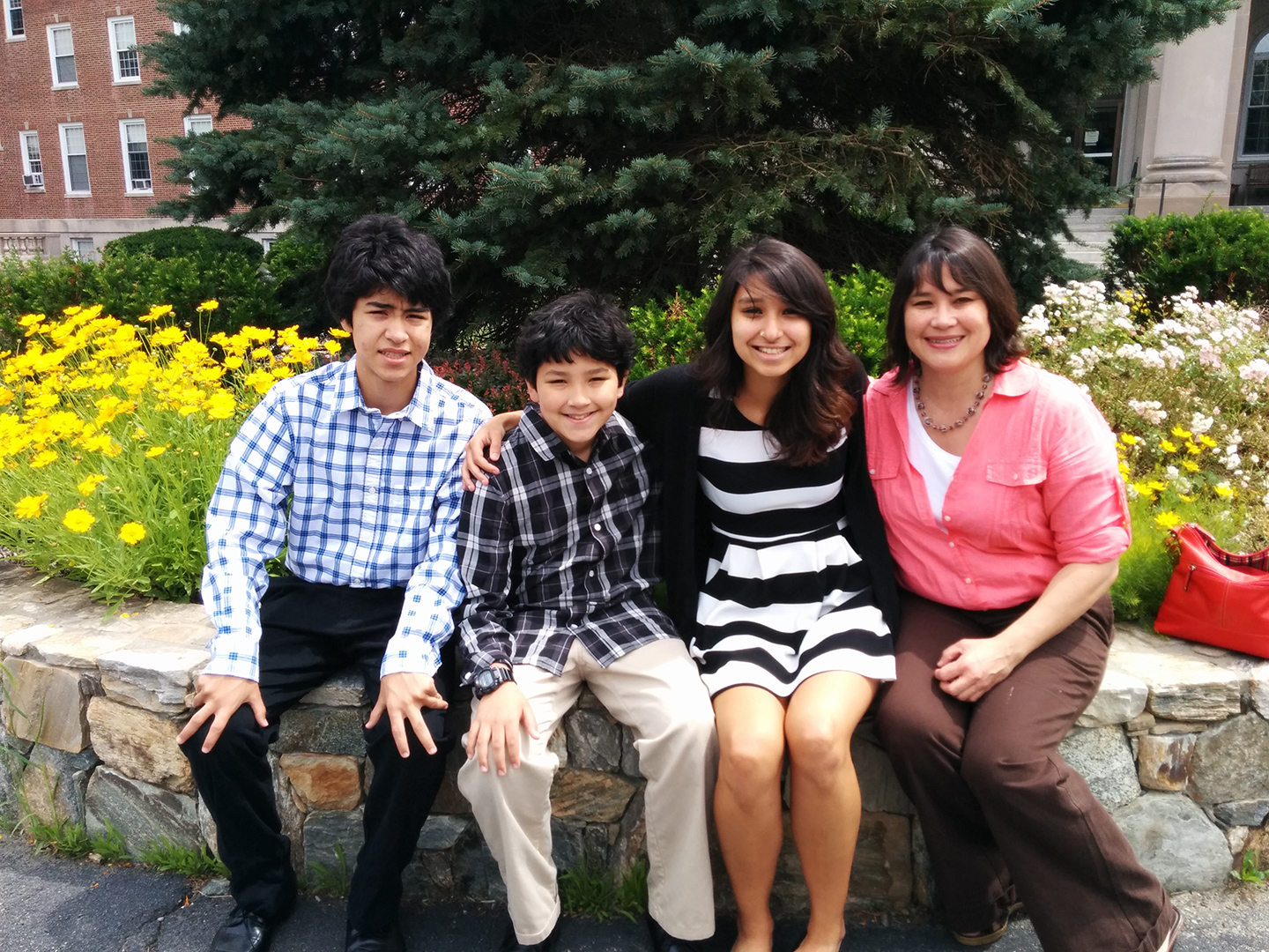 Kiki Tapiero sitting on stone wall with her two brothers and mother 