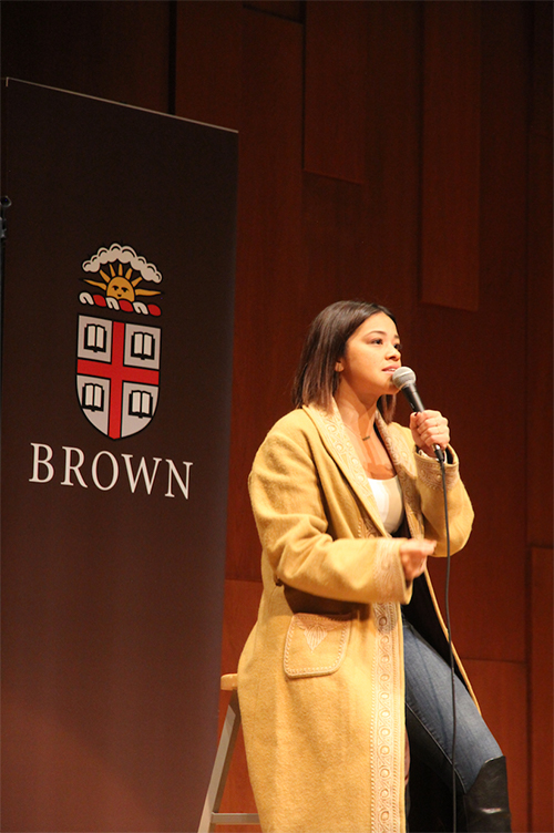 Gina Rodriguez sitting on stool on stage speaking at Brown
