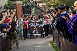 Students walk through the Van Wickle gates holding the Brown class of 2022 flag