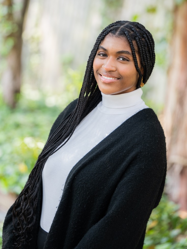 Cyprene stands in a white turtleneck and black sweater