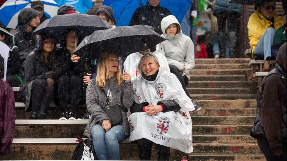 Football game spectators in bleachers under umbrellas in the rain