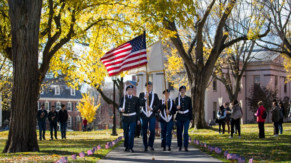 Color guard leading procession through the quad in dappled sunlight