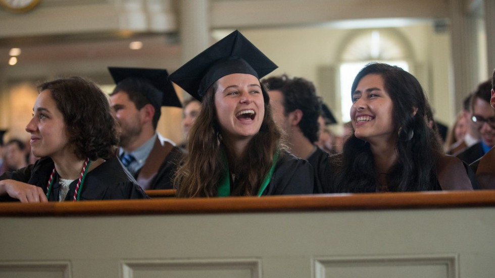 Graduates in caps and gowns sitting in pews, laughing