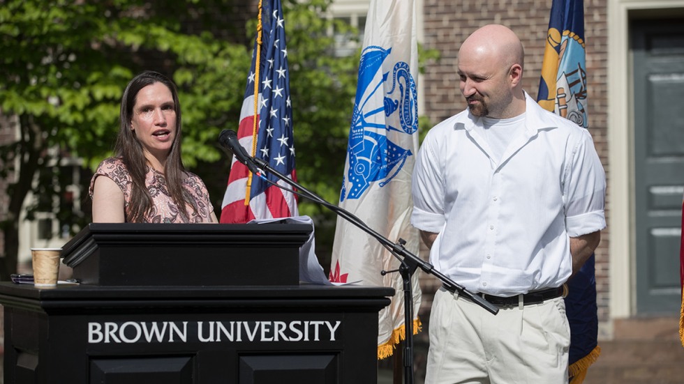 Christopher Baker standing on stage next to Karen McNeil speaking at podium