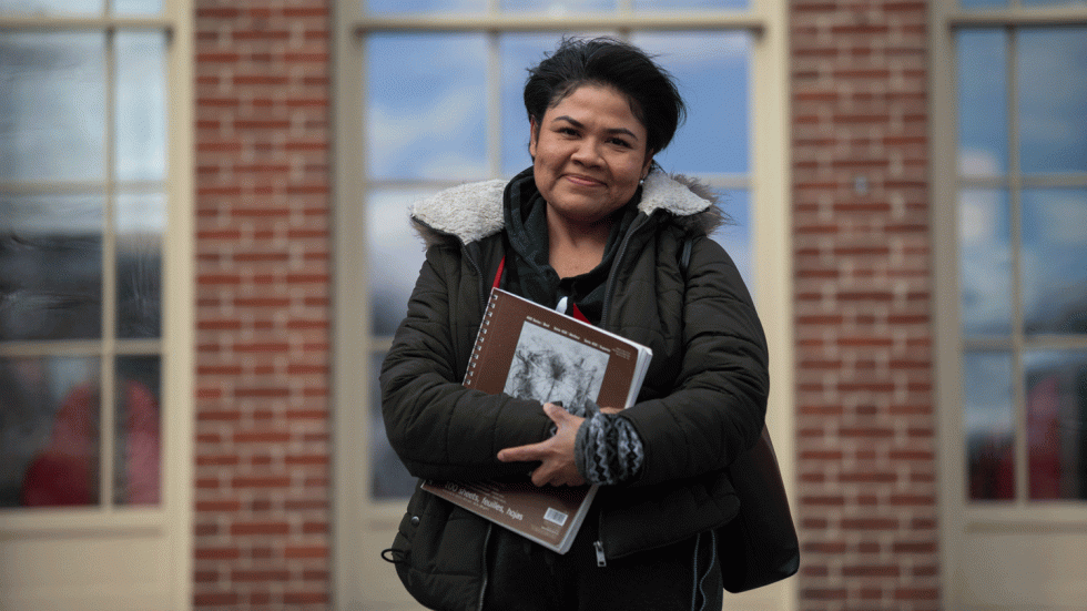 Viveka Ayala-Heredia standing in front of a brick building holding a sketchbook