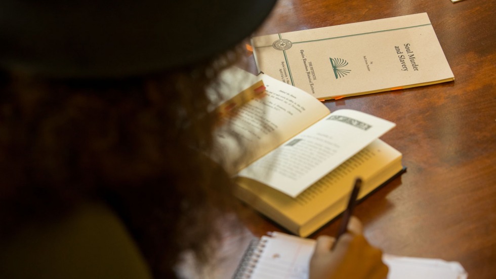 Student writing in a notebook surrounded by rare books about slavery in the Americas