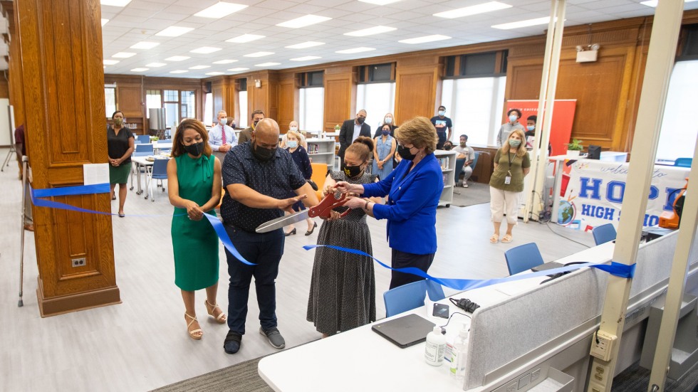 four people cutting a blue ribbon with large scissors