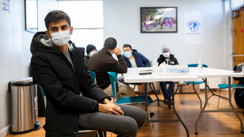 Man sitting near a folding table wearing a mask and a black coat