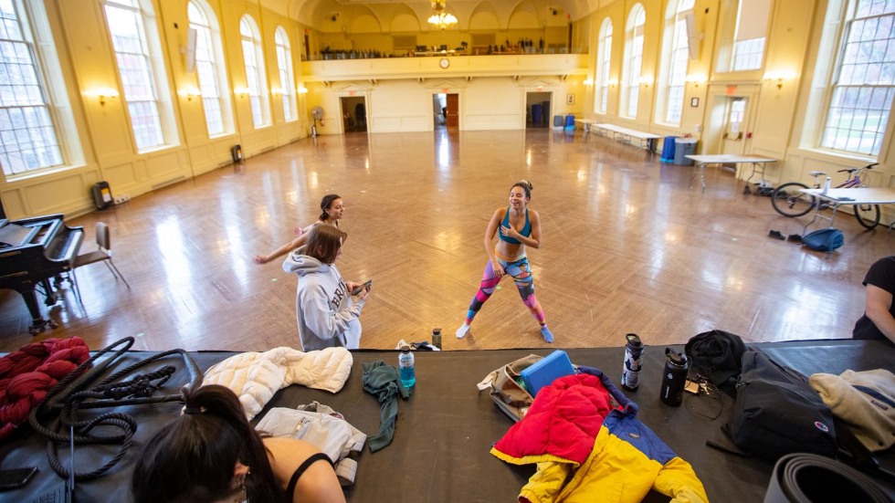 Students standing and laughing at the foot of a stage in a large ballroom