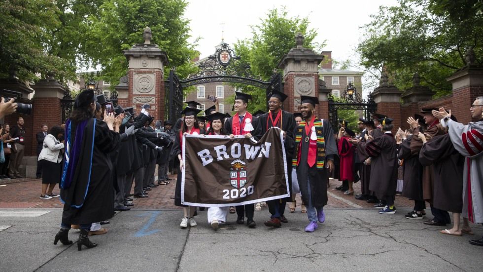 four people carrying a banner reading Brown 2020 and wearing graduation caps and gowns
