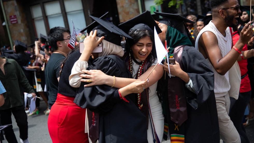 four people wearing mortarboard hats and graduation gowns hugging 