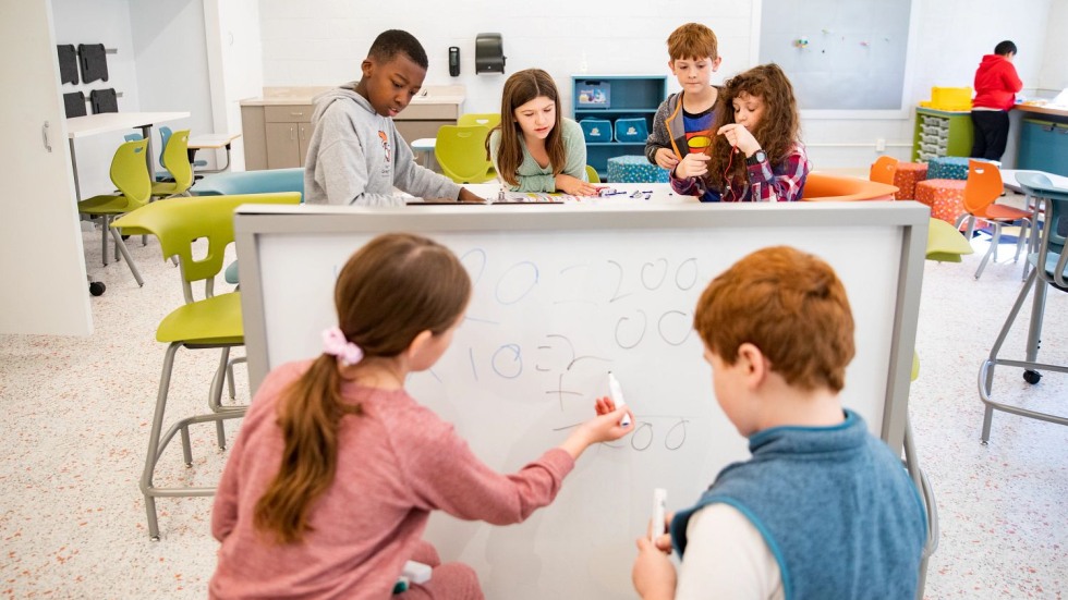 fourth grade students drawing math equations on a whiteboard