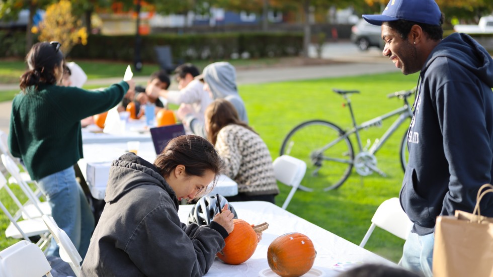 People paint pumpkins on tables outdoors.