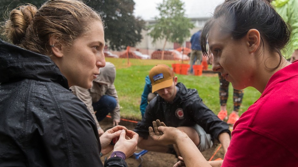 two people talking and holding artifacts at an archaeological dig site