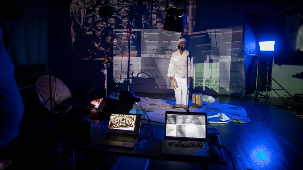 actor dressed as a U.S. Navy recruit standing in front of a projector