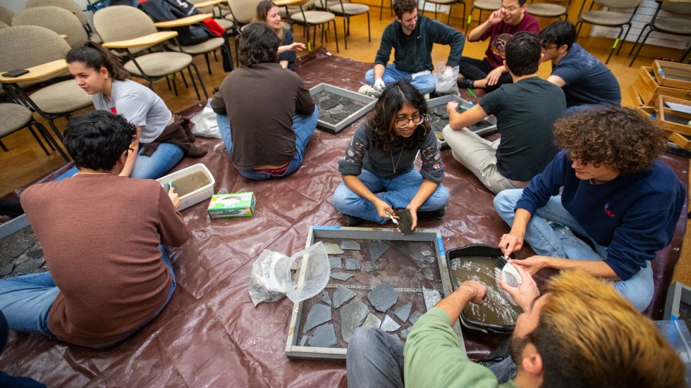 students sitting on a classroom floor cleaning archaeological artifacts