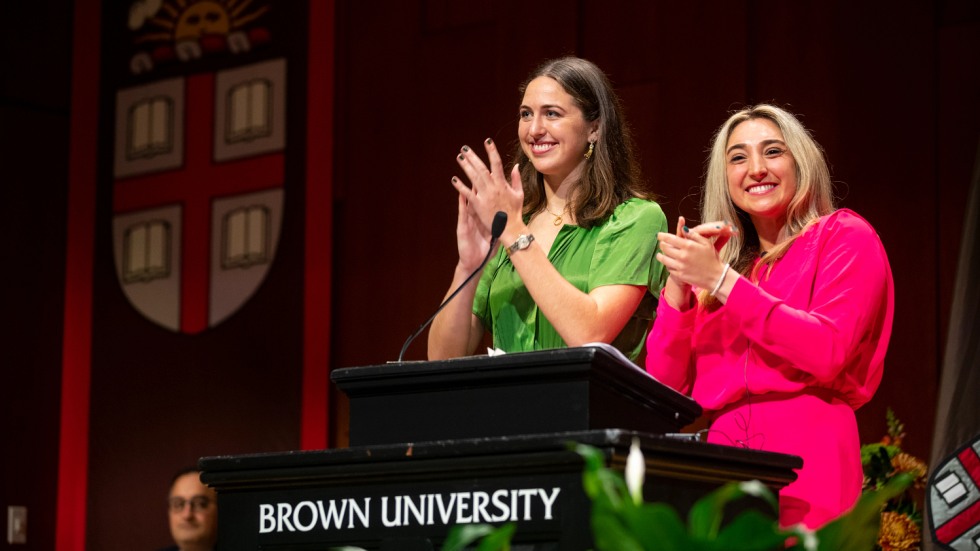 two students clapping and smiling at a podium