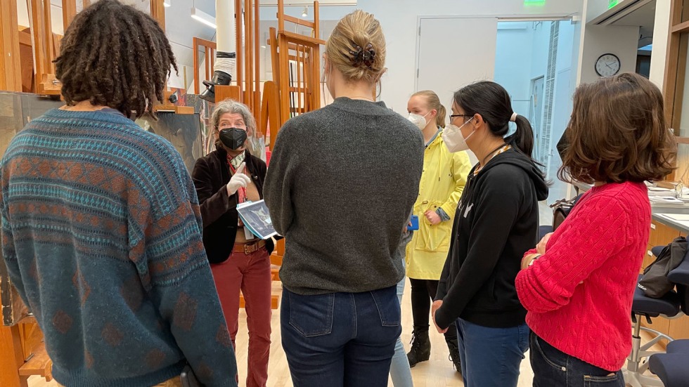 people gathered in a circle inside a museum conservation room talking with masks on