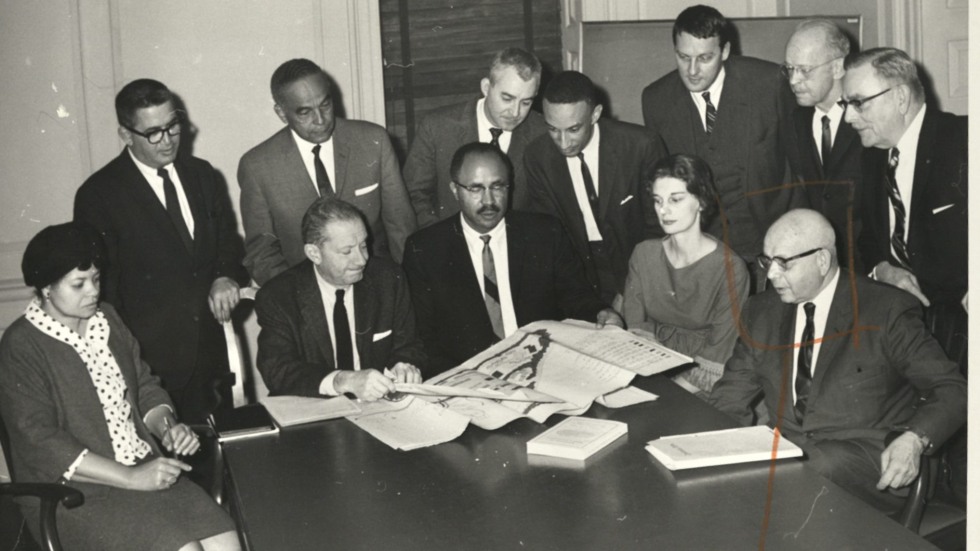 Black-and-white photo of people gathered around a conference room table