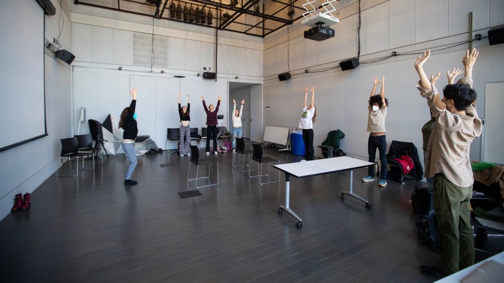 students standing in a half circle with arms raised above their heads