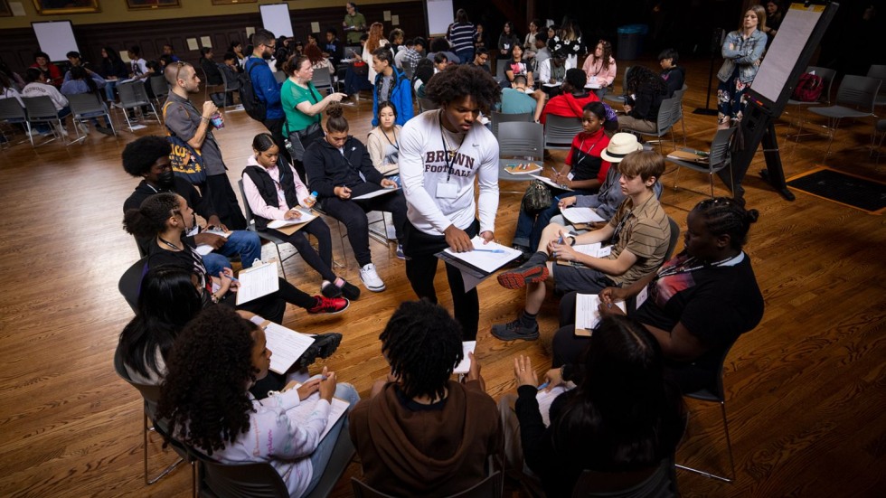 circle of seated middle school students speaking with a college student 