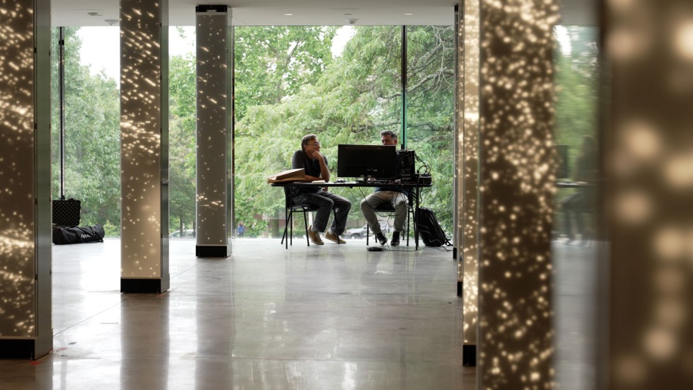 two people sitting at a desk with a computer, surrounded by LED-lit columns