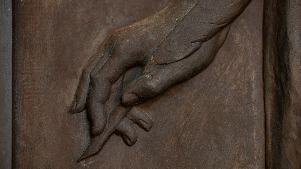 Bronze etching of hand holding a quill 