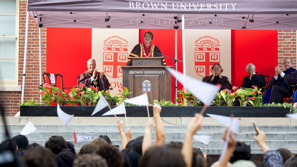 Christina Paxson standing at a podium with students waving pennants in the foreground