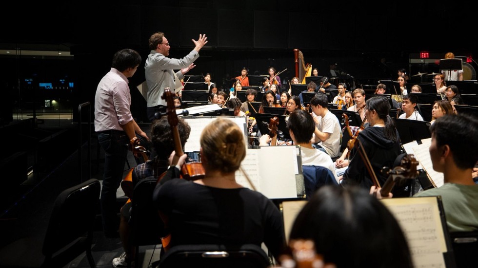 Eric Nathan and Mark Seto standing at a podium in front of the Brown Orchestra