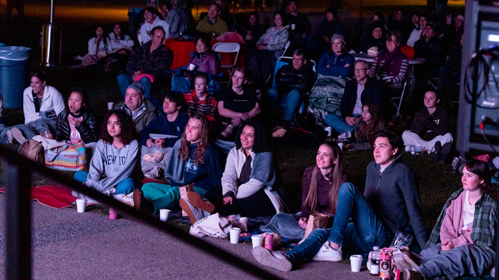 Students sit on the ground watching a movie