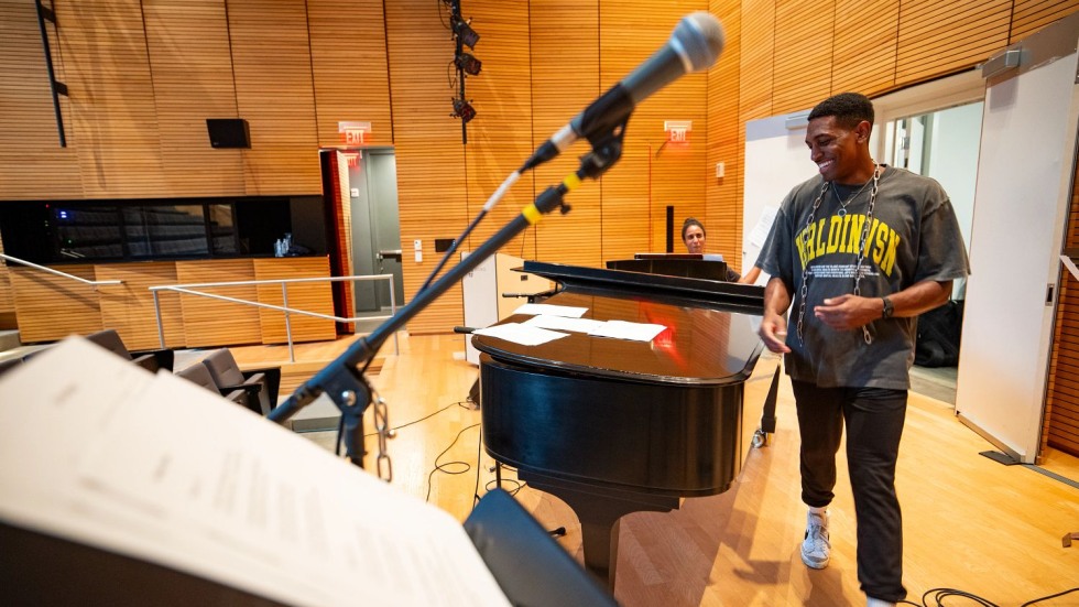 Marcus Grant smiling as he walks past a grand piano covered in sheet music