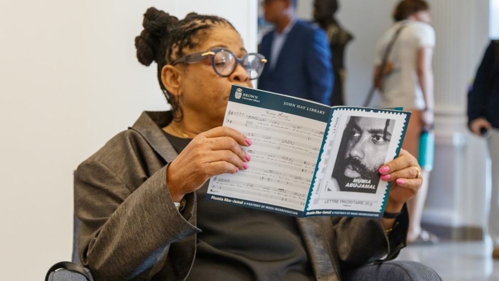 woman reading a paper program with Mumia Abu-Jamal's photo on the cover