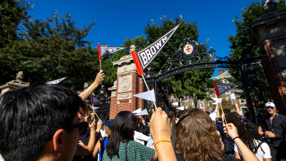 Students walking toward gates holding Brown flags