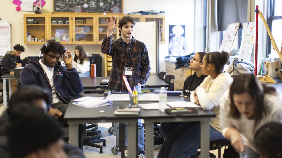 Brown graduate students leads a discussion among a table of high schoolers.