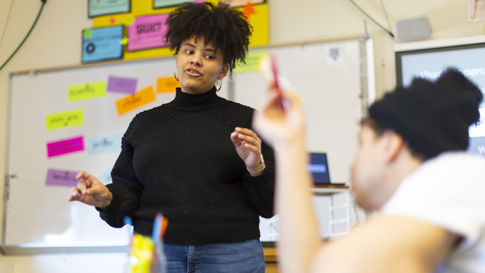 Brown graduate students leads a discussion among a table of high schoolers.